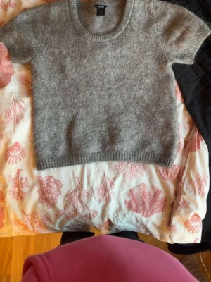 Grå stickad kortärmad tröja Lindex - Mysig grå stickad tröja från Lindex med korta ärmar och rund halsringning. Tröjan har en enkel, rak passform och ribbstickade kanter vid ärmslut och nederkant. Perfekt att styla lager på lager under kyliga dagar.