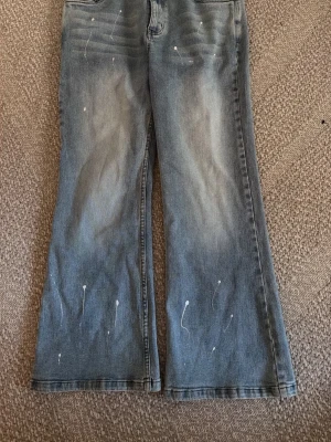 Gråblå bootcut jeans från 2KWRD - Snygga gråblå bootcut jeans från 2KWRLD med coola vita färgstänk och slitningar vid låren. Jeansen har klassisk femficksdesign och är tillverkade i denim. Perfekta för dig som gillar en avslappnad och trendig look. Nypris 749kr