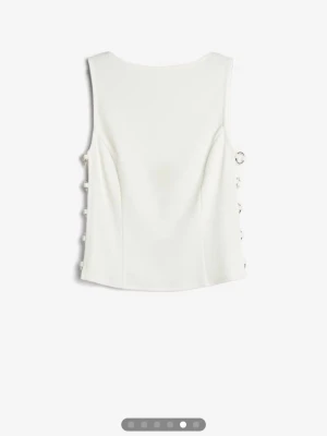 Vit linnetopp med ringdetaljer - Säljer en vit ärmlös linnetopp med unika silverfärgade ringdetaljer längs sidorna som ger en edgy look. Prislappen sitter kvar, säljer då den aldrig kommer till användning💕