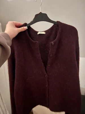 burgundy färgad kofta - Mysig kofta i burgundy färg. Koftan har rund halsringning, knappar framtill och lång ärm. Perfekt att slänga över en topp för en chill look.