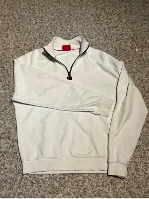 Vit halfzip från Hugo - Riktigt snygg vit halfzip-tröja från Hugo Boss med svart dragkedja o liten röd detalj på insidan av kragen. (Har en liten defekt som man kan ser på sista bilden men annars helt perfekt!) Hör av er vid frågor så svarar jag så snabbt jag kan👍Billigare vid snabb affär🫵