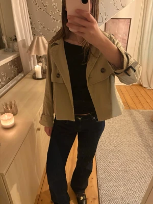 Kort beige trenchcoat med detaljer - Jätte fin i bra skick! OBS storlek 38 men liten i storleken skulle säga att den är mer en xs-s😊