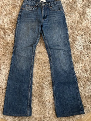 Blå utsvängda jeans från GinaTricot  - Säljer ett par klassiska blå jeans från GinaTricot med utsvängda ben och medelhög midja. Jeansen har fem fickor, bälteshällor och en snygg tvättad look. Tillverkade i slitstark denim som passar perfekt till en avslappnad stil. Jeansen är uppsydda några cm hos skräddare och passar perfekt för mig som är 163cm lång😊