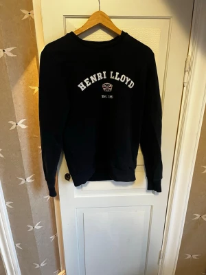Svart sweatshirt från Henri Lloyd - Klassisk svart sweatshirt från Henri Lloyd med tryckt logga och text på bröstet. Rund halsringning och ribbade muddar vid ärmslut och nederkant. Perfekt för en avslappnad och stilren look.