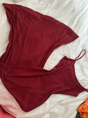 Vinröd långklänning med smala axelband - Säljer en vinröd långklänning med smala axelband och asymmetrisk nederkant. Klänningen har en enkel och stilren design, perfekt för dig som gillar minimalistiskt mode. Materialet känns mjukt och följsamt mot kroppen.