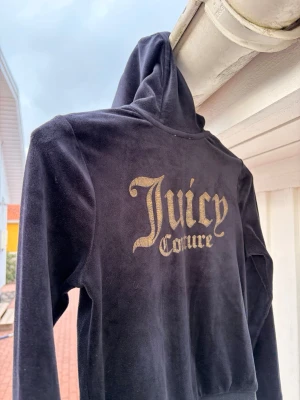 Svart velourtröja Juicy Couture - Svart hoodie från ✨Juicy Couture✨ i mjuk velour med guldigt tryck på både fram- och baksidan. Hoodien har huva, dragkedja och två fickor framtill. Perfekt för dig som gillar klassisk Y2K-stil 🌟och vill ha något riktigt comfy. Strl 8/9 men är som xxs/xs. 