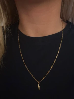 Guldhalsband med blixtberlock - Snyggt halsband i guld med en tunn kedja och en liten blixtformad berlock. Perfekt för dig som gillar minimalistiska smycken med en cool twist. Passar till många olika stilar och är lätt att matcha med andra accessoarer.