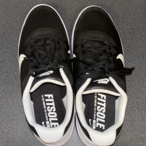 Nike Fitsole golf skor svartvita sneakers - Säljer ett par snygga svartvita Nike Fitsole golf skor med klassisk vit swoosh på sidan. Skorna har lågt skaft, svarta snören och vit innersula med Fitsole-tryck. Yttermaterialet är syntet och sulan har mönster för extra grepp.