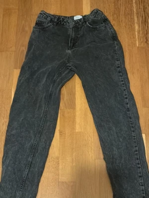 Svarta mom jeans från Grunt - Säljer ett par svarta mom jeans från Grunt med tvättad look. Jeansen har hög midja, raka ben och klassisk femficksdesign. Tillverkade i ekologisk bomull för en skön och hållbar känsla. Perfekta för en avslappnad och trendig stil.