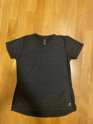 Svart tränings-tshirt från SOC - Snygg svart tränings-tshirt från SOC med diskret mönster och V-ringning. Tillverkad i ett lätt och snabbtorkande material som passar perfekt för gymmet eller löprundan. Kort ärm och logga nere vid fållen.