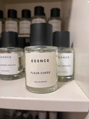 ESSNCE Fleur Chere Eau de Parfum - Obs! Läcker pyttepyttelite när flaskan ligger ner, därav pris.  Minimalistisk parfym från ESSNCE med doften Fleur Chere. Flaskan är cylindrisk i genomskinligt glas med svart matt kork och vit etikett med stilren text. Perfekt för dig som gillar enkla och moderna doftflaskor.