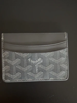 Grå kortfodral  - Snyggt grått kortfodral med det klassiska mönstret och vita detaljer. Fodralet har flera fack för kort och är tillverkat i canvas med läderdetaljer. Perfekt för dig som vill ha en stilren och exklusiv accessoar.