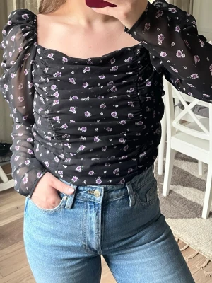 Svart blommig mesh blus med puffärm - Svart blus med små blommor, puffiga långärmar i mesh och rynkade detaljer. Fyrkantig urringning och figurnära passform. Kan kläs upp och ned. 