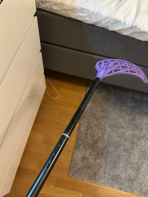 Innebandyklubba med lila blad unihoc ewolabe  - Säljer en innebandyklubba från Evo med svart skaft och ett lila plastblad. Skaftet har en stilren design med diskreta detaljer och bladet är lätt och luftigt med ett öppet mönster. Perfekt för dig som gillar innebandy och vill ha en snygg klubba.