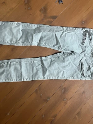 Gravidbyxor från Heartbeats - Snygga ljusgrå gravidbyxor från Heartbeats med klassisk femficksmodell och dragkedjor på fickorna. Jeansen har smal passform och är tillverkade i stretchigt denimtyg för extra komfort. Perfekta för en trendig och avslappnad stil.