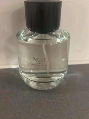 Zara Nuit Night Collection parfym - Zara Nuit Night Collection parfym i en rund, genomskinlig glasflaska med svart lock. Flaskan har en stilren och modern design med enkel text på framsidan. Perfekt för dig som gillar eleganta och minimalistiska doftflaskor.