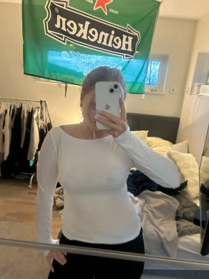 Vit långärmad topp med bred ringning - Säljer en stilren vit långärmad topp med bred, rundad ringning. Toppen har en tight passform och är perfekt att matcha med både jeans och kjol. Enkel och clean design utan synliga detaljer eller mönster.