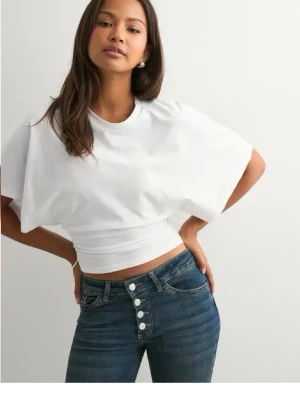 Vit croppad topp med vida ärmar - Säljer en vit croppad topp med vida korta ärmar och tight midja. Toppen har en modern och stilren look, perfekt att matcha med höga jeans. Materialet känns mjukt och stretchigt, troligen bomull eller polyester.