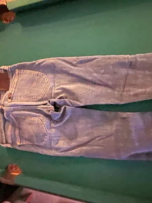 Blå raka jeans med läderpatch - Säljer ett par klassiska blå jeans med raka ben och femficksmodell. Jeansen har en snygg läderpatch bak i midjan och kontrastsömmar. Perfekta till en avslappnad stil och tillverkade i slitstarkt denimtyg.