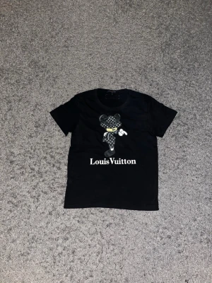 Lw tröja - Snygg svart t-shirt från Lw med ett stort tryck av en tecknad figur på framsidan och tydlig logga under. Klassisk rund hals och korta ärmar. Perfekt för dig som vill sticka ut med en exklusiv streetwear-look.