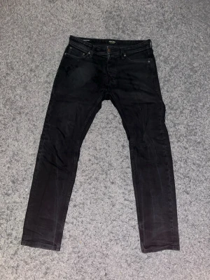Jack & Jones - Snygga svarta slim fit jeans från Jack & Jones med klassisk femficksdesign och knappgylf. Jeansen har raka ben och diskreta sömmar, perfekta till en avslappnad streetstil. Materialet är mjukt denim i bomull med lite stretch för extra komfort.