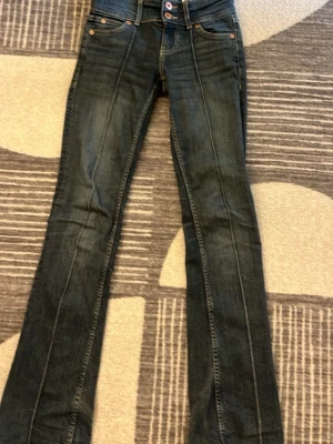 Mörkblå bootcut jeans med kontrastsömmar - Snygga mörkblå bootcut jeans med kontrastsömmar och klassiska femficksdetaljer. Jeansen har en hög midja och subtila slitningar på benen. Perfekt för dig som gillar en tidlös och cool look. Materialet är denim.