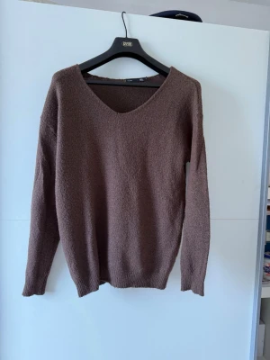 Brun stickad tröja med v-ringning - Mysig brun stickad tröja med djup v-ringning och långa ärmar. Tröjan har en enkel, avslappnad passform och ribbade muddar vid ärmslut och nederkant. Perfekt för lager på lager och en chill look.