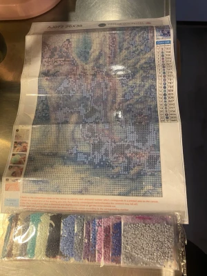 Diamond painting kit med vargmotiv - Säljer ett diamond painting kit från French Pyssel med motiv av en varg i skogen. Kitet innehåller en canvas på 26x36 cm och flera påsar med små färgglada plastdiamanter i blå, lila, grå och turkosa nyanser. Perfekt för dig som gillar pyssel och kreativa projekt.