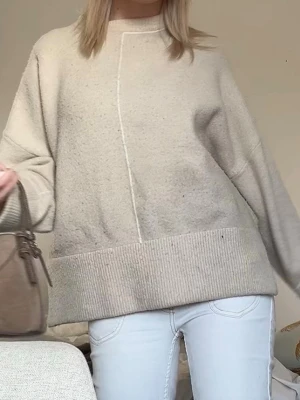 Beige oversized stickad tröja - Säljer en beige oversized stickad tröja med bred ribbad kant nedtill och vid ärmslut. Tröjan har en rak passform och en dekorativ söm framtill. Perfekt för lager på lager och chill stil. Den är lite nopprig men det går bort me en sån här maskin. 