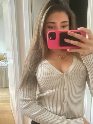 Beige ribbad kofta med v-ringning - Trendig beige ribbad kofta med v-ringning och knappar framtill. Långärmad och figurnära modell som passar perfekt till jeans eller kjol. Mjuk och stretchig!