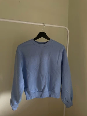 Ljusblå sweatshirt utan huva - En stilren ljusblå sweatshirt i mjukt material. Tröjan har rund halsringning, ribbade muddar vid ärmslut och nederkant samt en relaxed passform. Perfekt för en chill och enkel look.
