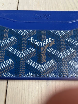 Blå korthållare - Snygg blå korthållare med det klassiska mönstret i vitt och brunt. Tillverkad i canvas och läder, har flera fack för kort och är perfekt för dig som vill ha något både stilrent och unikt. Märket och Paris står tryckt på framsidan. 