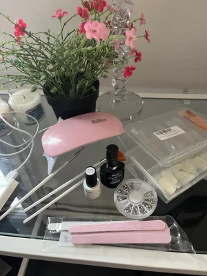 Gelnaglar set - Ett kit (ej komplett) med tillbehör för att göra egna gelnaglar.  Innehåller:  - En mini uv lampa - Nageltippar, genomskinliga och vita (inte alla kvar)  - Top gel lack (ungefär hälften kvar) - Beige/ dammrosa gel lack (lite kvar)  - Glitterstenar - Engångs sandpapper filar - Borstar