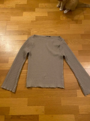 Beige långärmad topp från 157 - Säljer en beige långärmad topp från 157 i våfflad struktur. Toppen har en enkel, rak passform och är tillverkad i ett mjukt material som känns skönt mot huden. Perfekt att styla med jeans eller kjol för en clean look. Tror inte toppen är använd, isåfall endast någon gång. Har katter hemma!!!