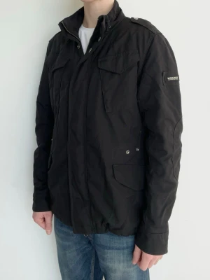 Woolrich Field Jacka Svart - Snygg och eftertraktad field jacka från Woolrich! Fint skick inga defekter. Storlek M (EU), modellen är ca 182, 70kg. Kontakta mig för fler frågor och funderingar!