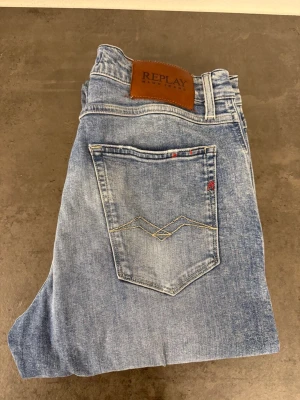 Ljusblå jeans från Replay W32 - Snygga ljusblå jeans från Replay med klassisk femficksmodell och diskreta slitningar. Jeansen har raka ben och en läderpatch med Replay-logga bak i midjan. Materialet är mjukt denim med en tvättad look och kontrastsömmar på bakfickan.
