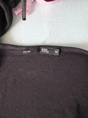 Svart omlottopp 157 - Svart omlottopp från 157 med långa ärmar och knytband i midjan. Toppen har en mjuk och stretchig känsla, perfekt för en avslappnad men ändå snygg look. Passformen är normal och tyget är tunt och luftigt