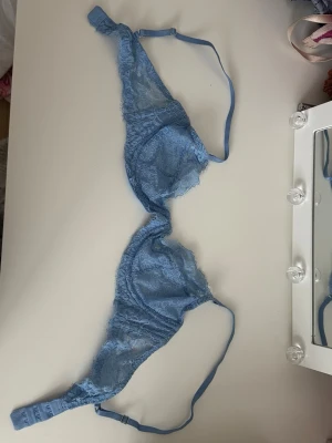 Blå spets-bh med tunna band - Söt blå bh i genomskinlig spets med tunna axelband och justerbar knäppning bak. Bh:n har triangelformade kupor och fina spetsdetaljer som ger en romantisk känsla. Perfekt för dig som gillar en lätt och luftig stil.