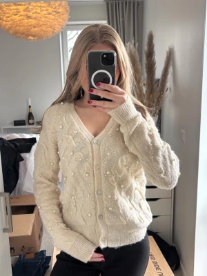 Krämvit kofta med pärldetaljer - Säljer en krämvit kofta med v-ringning och dekorativa pärlor över hela plagget. Köpt på Zara i storlek S. Använd väldigt få gånger därav inga tecken på användning.