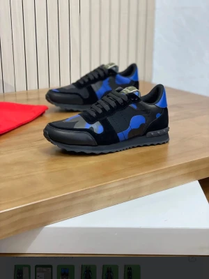 Valentino blå och svarta sneakers - Snygga sneakers från Valentino med blå och svarta kamouflagemönster. Skorna har svarta snören, svarta detaljer i mocka och textil samt en robust sula med mönstrat grepp. Perfekta för dig som vill sticka ut med en cool och modern stil.