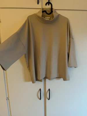 Beige oversized tröja från Carin Wester - Säljer en beige oversized tröja från Carin Wester med hög krage och vida trekvartsärmar. Tröjan har en avslappnad passform. Perfekt för en chill och stilren look. Använd ett fåtal gånger. Katt finns i hemmet.
