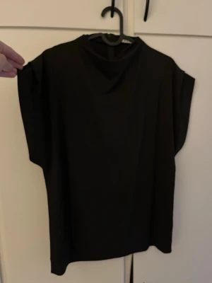 Svart loose topp med hög hals - En svart supersöt topp med hög hals och ärmlös design. Enkel och stilren modell som passar till det mest. Från Wera. Katt finns i hemmet!
