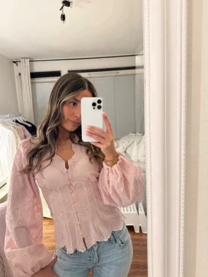 balloon sleeve blouse  - Söt ljusrosa blus med broderade blommor och knappar framtill. Blusen har v-ringning med vågig kant och långa puffärmar med resår vid handlederna. Tillverkad i ett tunt, luftigt tyg som ger en romantisk känsla. Helt ny med prislappen kvar. Slutsåld!
