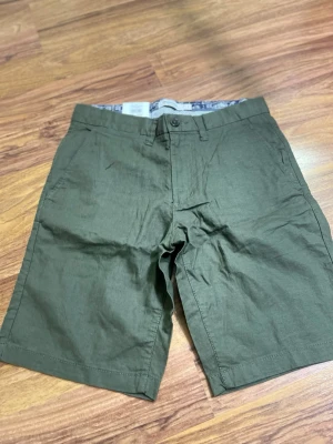 Olivgröna linneshorts från Dressmann - Snygga olivgröna shorts från Dressmann i en skön linneblandning. Klassisk modell med knapp och dragkedja framtill samt sidfickor. Perfekta för varma dagar och enkel att matcha med t-shirt eller skjorta.