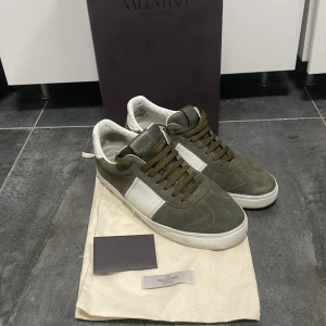 Valentino flycrews  - Snygga Valentino flycrews i olivgrön mocka med vita detaljer. Skorna har snörning och en klassisk design som passar perfekt för en stilren look. Ungefär 5 nitar borta