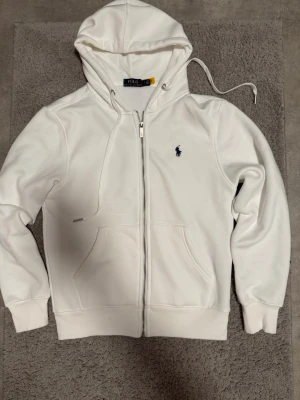 Polo Ralph Lauren ziphoodie svart/vit - Två snygga ziphoodies från Polo Ralph Lauren, en i vitt och en i svart. Båda har dragkedja, huva med dragsko och klassisk broderad logga på bröstet. Mjukt material och kängurufickor framtill. Perfekt för en chill och stilren look.