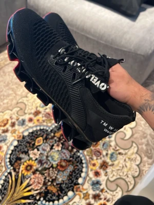 Svarta sneakers med röd sula - Svarta sneakers från TM Will med stickad ovandel och cool textdetalj på plösen. Skorna har en unik, vågig sula i svart med röda detaljer undertill och svarta skosnören. Ovandelen är i mesh för bra andningsförmåga och sportig känsla.