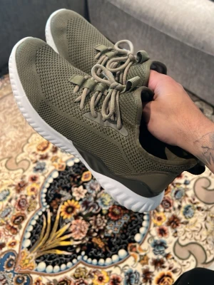 Olivgröna sneakers med vit sula - Snygga olivgröna sneakers med stickad mesh-ovandel och vita, räfflade sulor. Skorna har klassisk snörning och sportig design som passar perfekt till streetwear. Materialet är lätt och andas, vilket gör dem bekväma hela dagen.