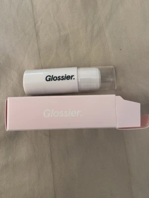 Glossier Haloscope highlighter stick - Glossier Haloscope highlighter i färgen Moonstone. Kommer i en smidig stickform med vit hylsa och genomskinligt lock. Ger en fräsch, daggig glow till huden. Förpackningen är ljusrosa och vit, perfekt att ha med i väskan.