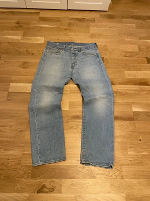 Levi's ljusblå 501 jeans  - Klassiska ljusblå jeans från Levi's. Jeansen har en vintagekänsla med subtila slitningar och är tillverkade i 100% bomull. Perfekta för en avslappnad och tidlös stil. Vill också på peka att det finns ett hål som du kan se i bilderna 